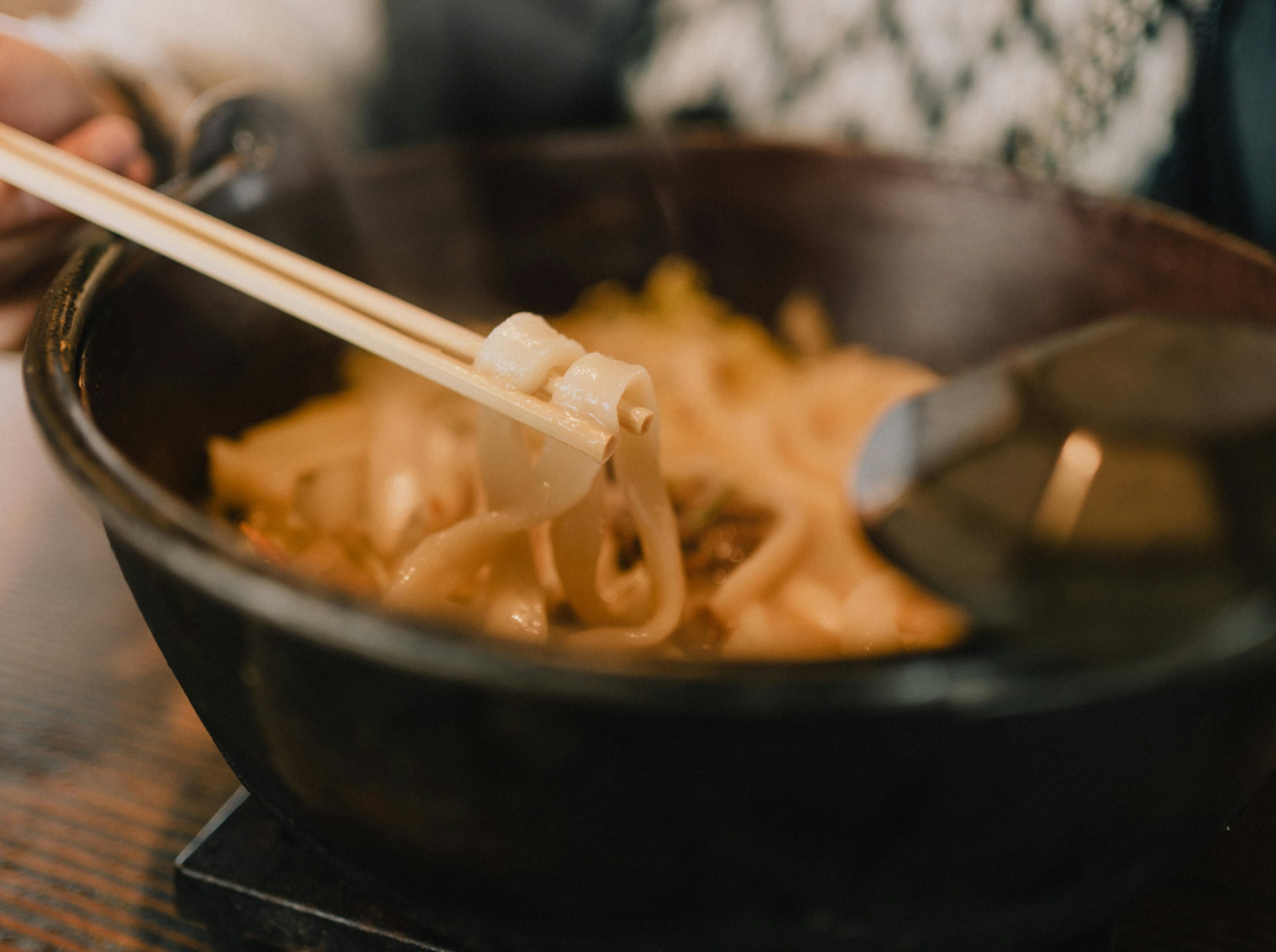 Close-up of steaming udon noodles in a bowl with chopsticks, perfect for a cozy meal.