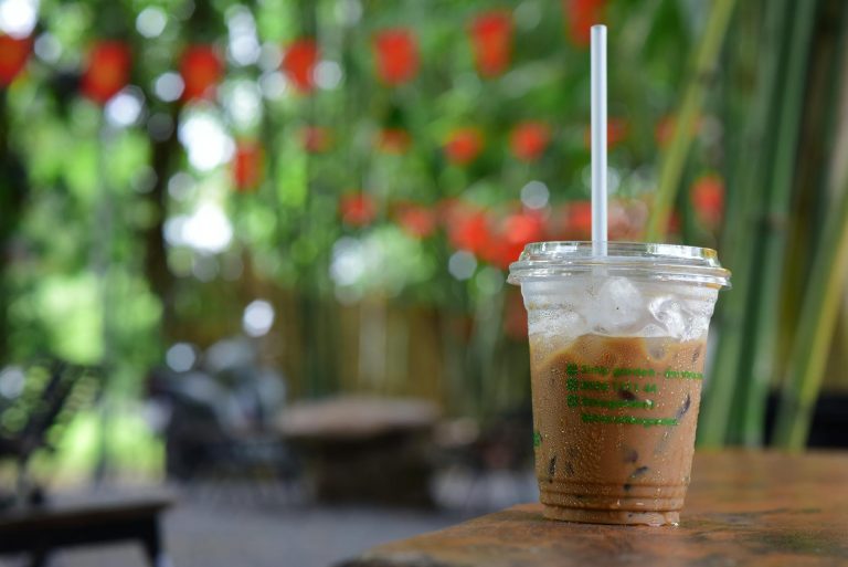 Close-up of iced coffee in a plastic cup on a table in a vibrant outdoor cafe with greenery and deco
