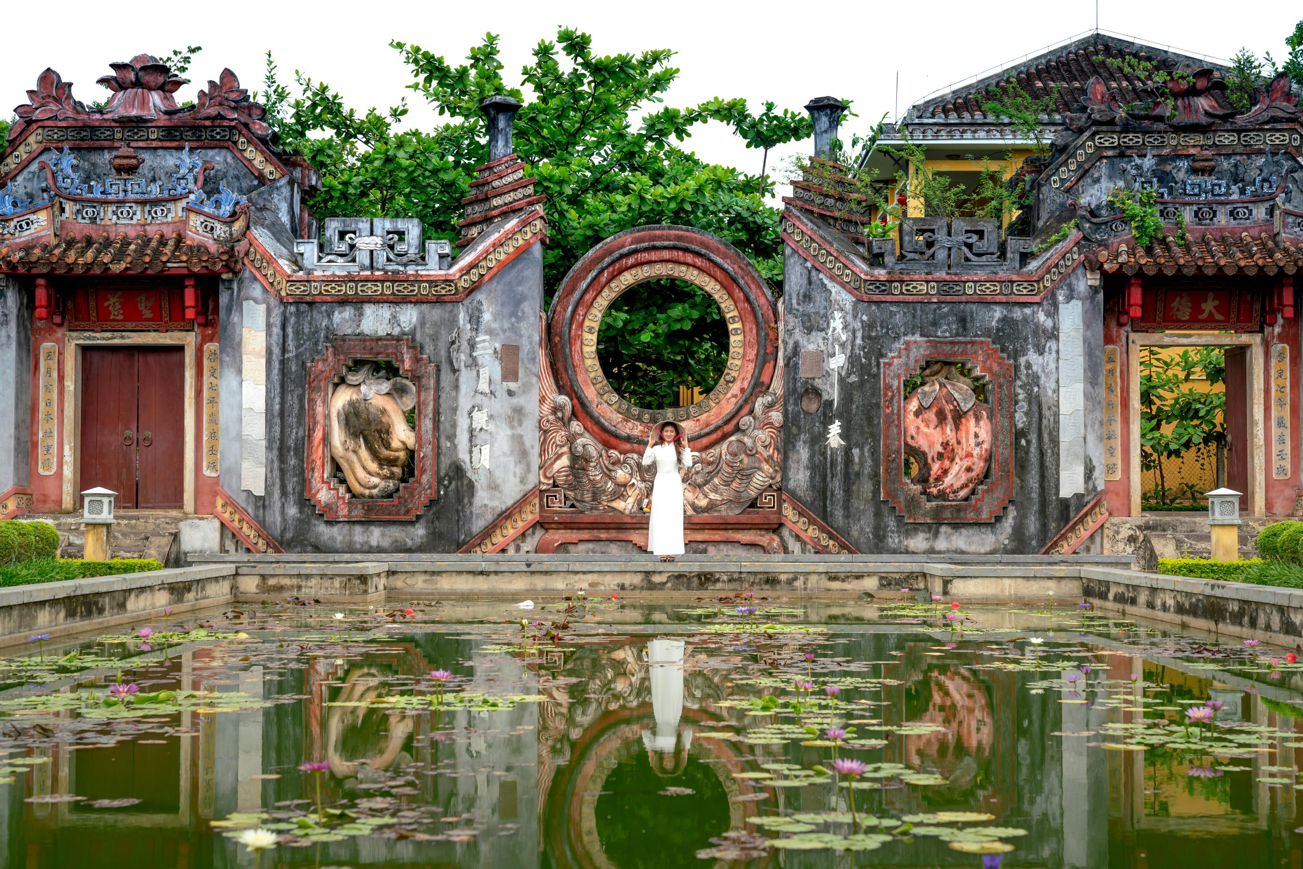 Woman in traditional attire stands by a temple pond, reflecting cultural heritage and serene surroundings.