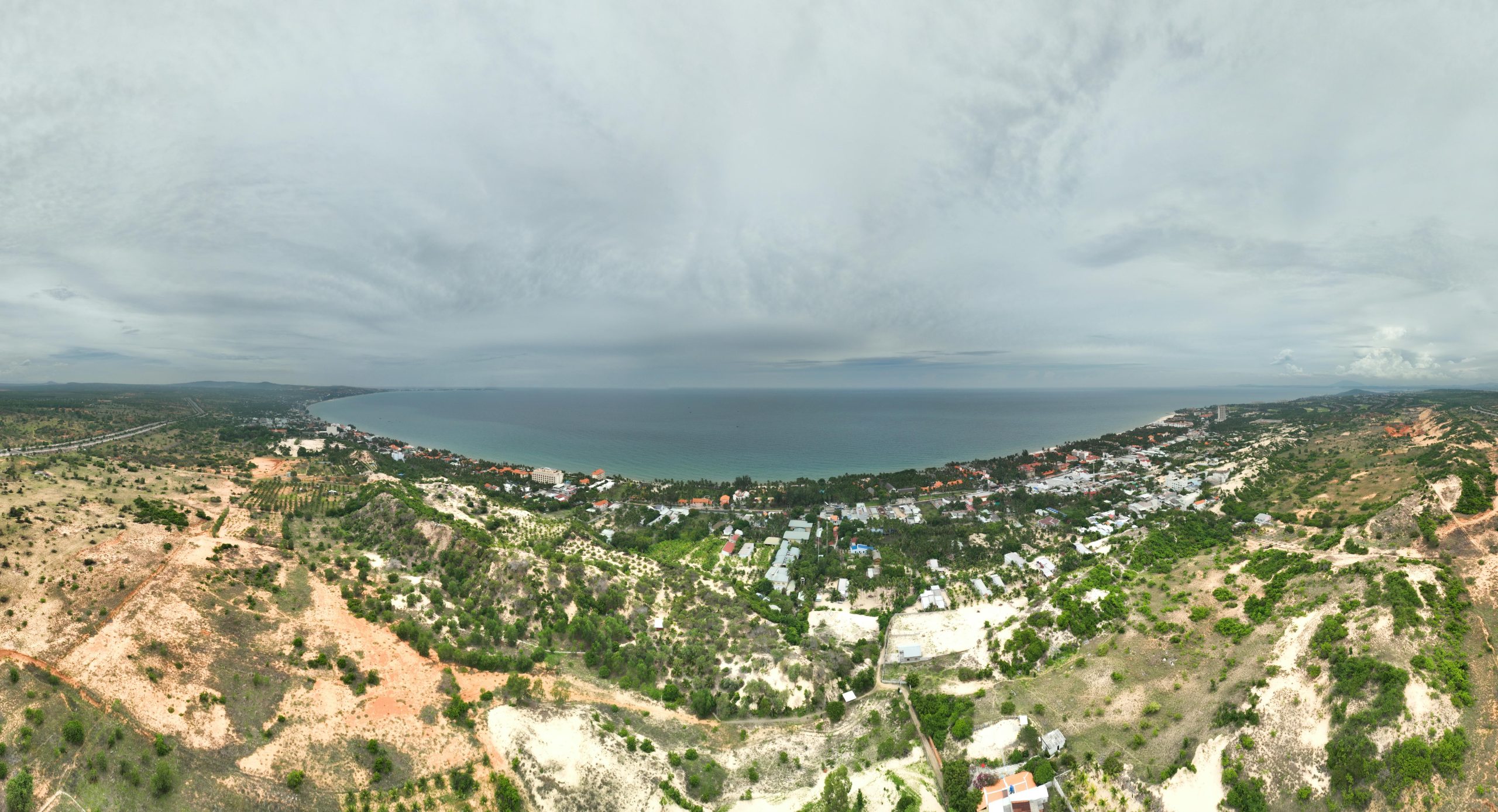 Expansive aerial view of a coastal town overlooking the sea under an overcast sky, showcasing natural landscapes and urban areas.