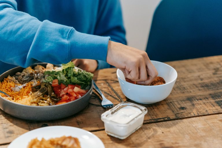 Crop anonymous male in blue sweatshirt having delicious dinner at timber table in kitchen