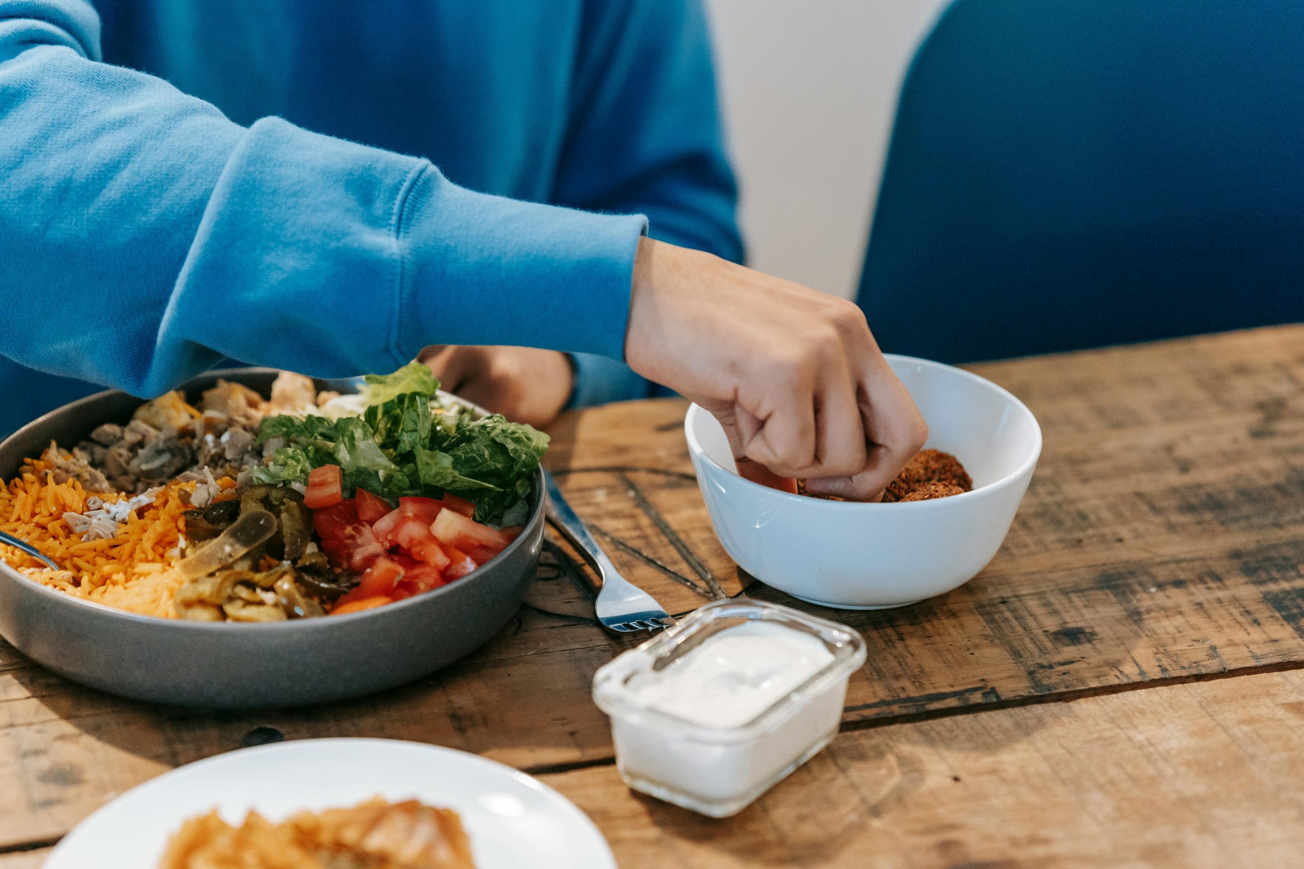Crop anonymous male in blue sweatshirt having delicious dinner at timber table in kitchen